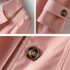 Nahaufnahme einer rosa Jacke mit hochgekrempelten Ärmeln und einem dekorativen Knopf, der die Stoffstruktur hervorhebt.