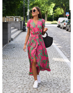 Eine Frau trägt ein rot-grünes Sommerkleid, dazu weiße Schuhe und eine schwarze Handtasche